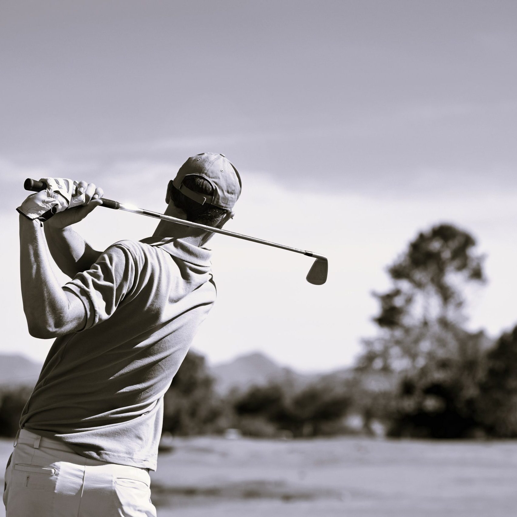 A man mid golf swing looking over the course to watch his ball land